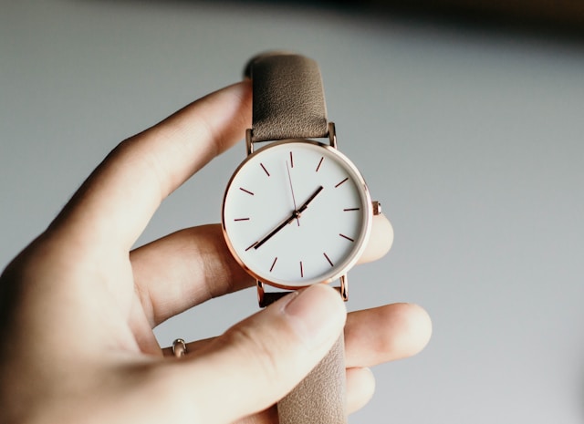 a hand holding a watch with a beige wristband